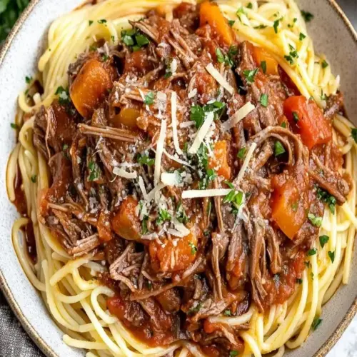 Slow cooker beef ragù served with pasta and garnished with fresh basil