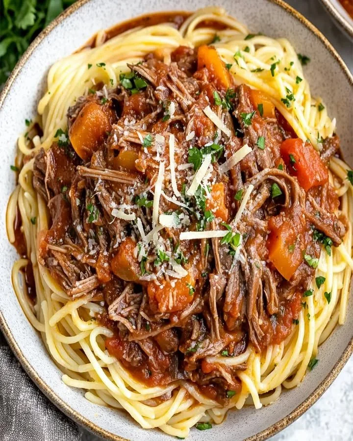 Slow cooker beef ragù served with pasta and garnished with fresh basil